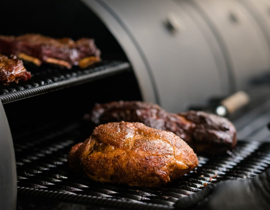 Seasoned barbecue cuts smoking on grates inside a professional offset smoker
