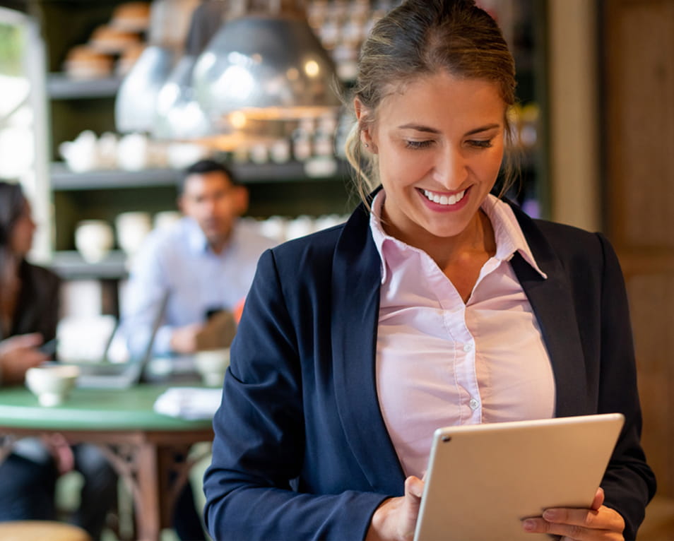 Smiling restaurant manager using a tablet in a bright modern cafe with guests in the background