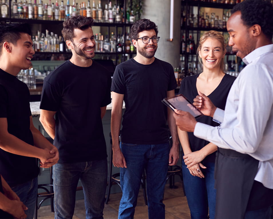 Restaurant manager training front-of-house staff with a tablet POS at the bar