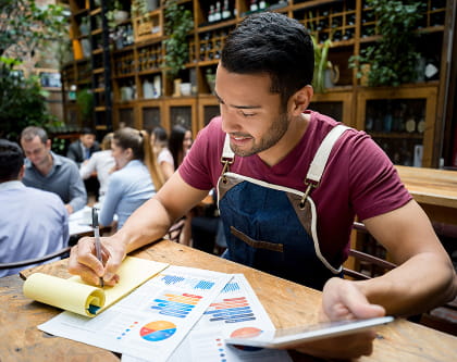 Restaurant operator reviewing charts on a tablet and notepad at a dining-room table